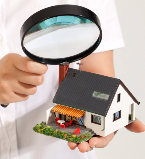 female hand holds a magnifying flass over a miniature house